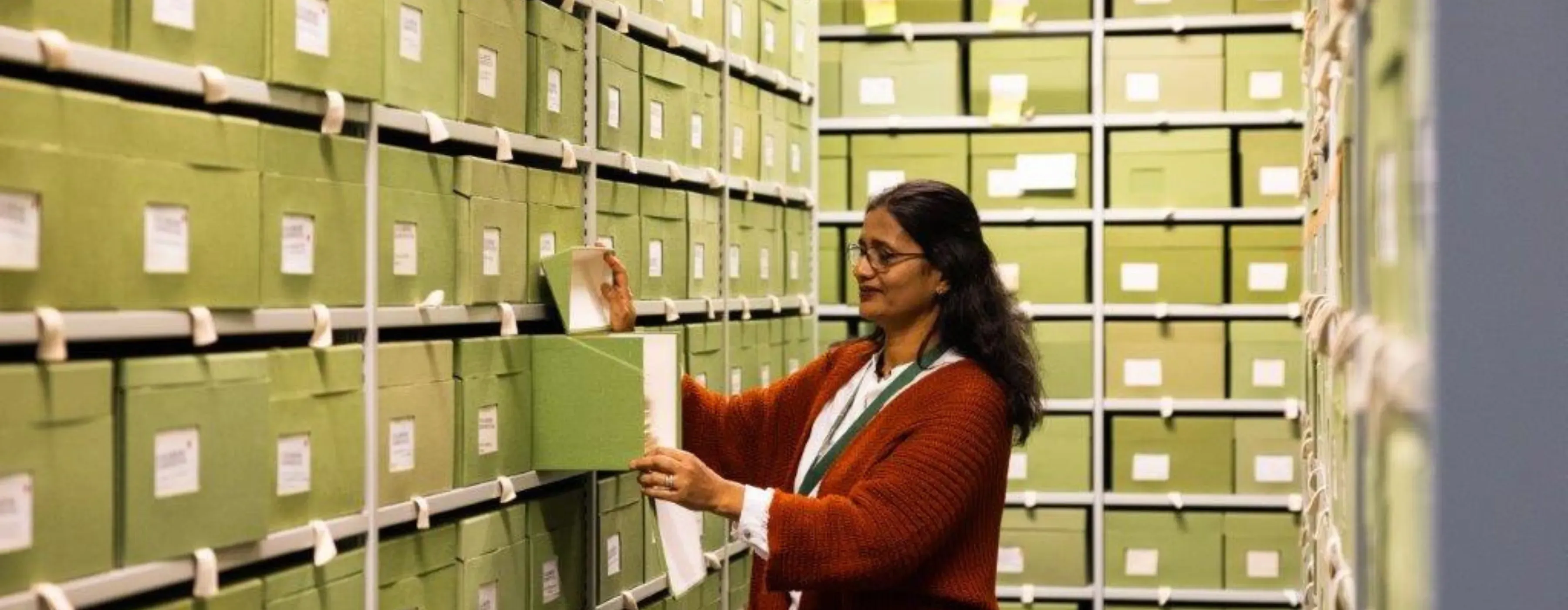 Researcher retrieving specimens from Kew’s Fungarium A woman selects a specimen box from a shelf filled with green archival boxes at Kew’s Fungarium.