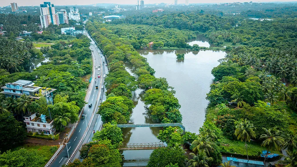 An aerial view of the Sarovaram Biopark, the destination for the orchids in this pilot study that have been rescued from destruction © Kerala Tourism A landscape rich with green trees, a lake, a busy road and a few highrise buildings.