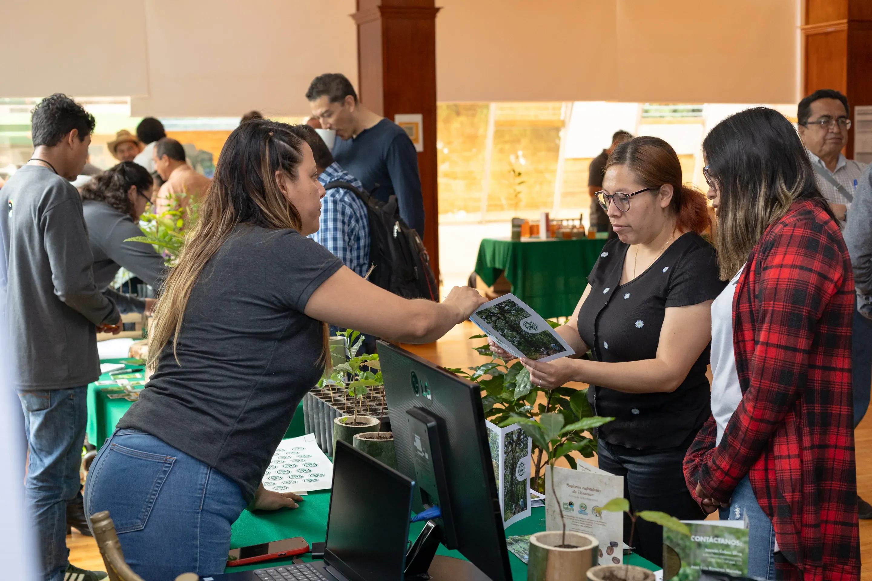 Engaging with communities: Farmers and stakeholders participate in one of the project’s training workshops, exchanging knowledge on sustainable management practices and biodiversity conservation © Alejandro Guerrero Three women stand around a counter covered in plants and a computer. One woman is talking to the other two about the contents of a training manual