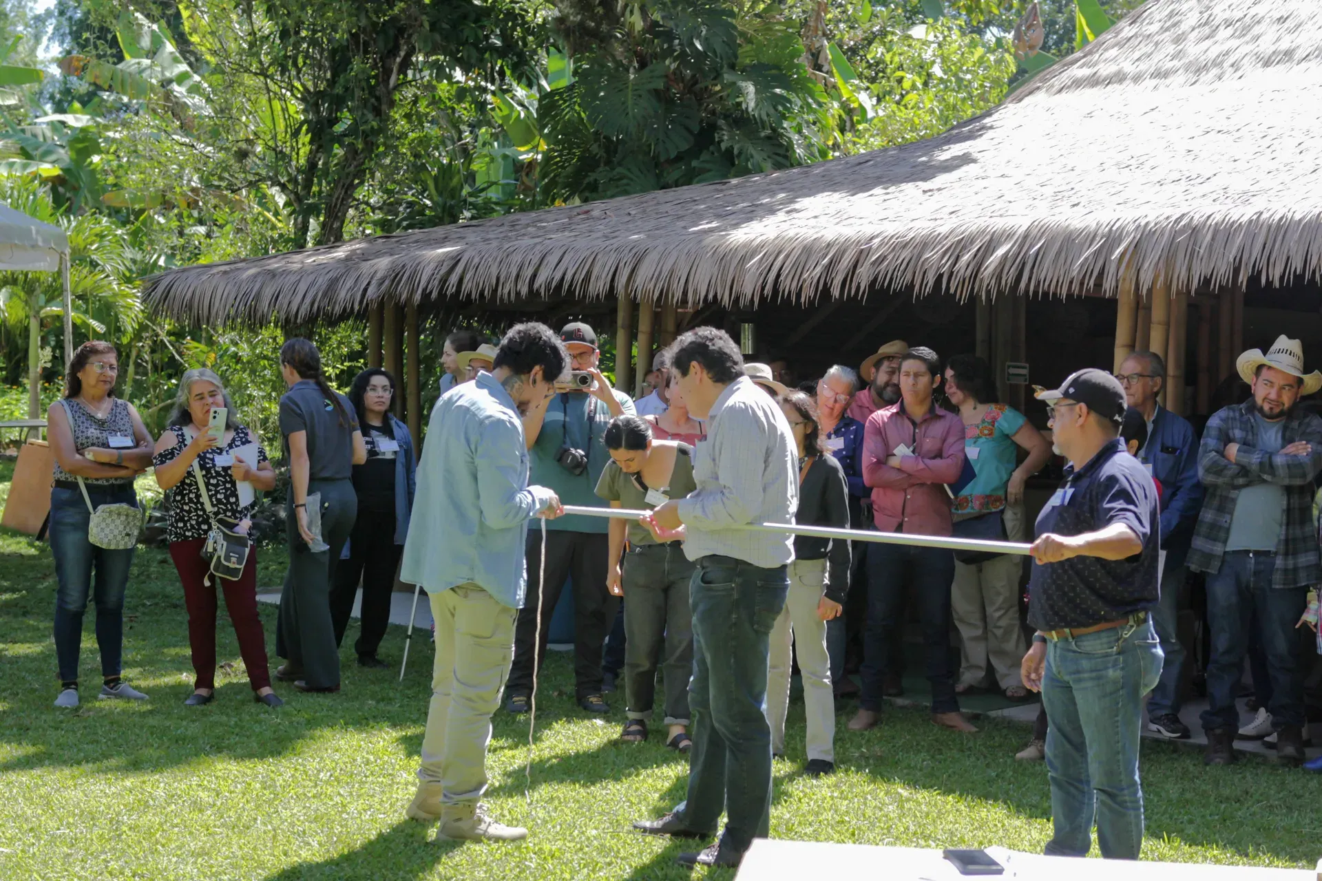 Learning by doing – Farmers and experts engage in hands-on training building skills to monitor carbon capture and to implement sustainable land management practices © Alejandro Guerrero A small group of people are being trained to use some specialist kit while a larger group of onlookers watch from the shade cover of an open building