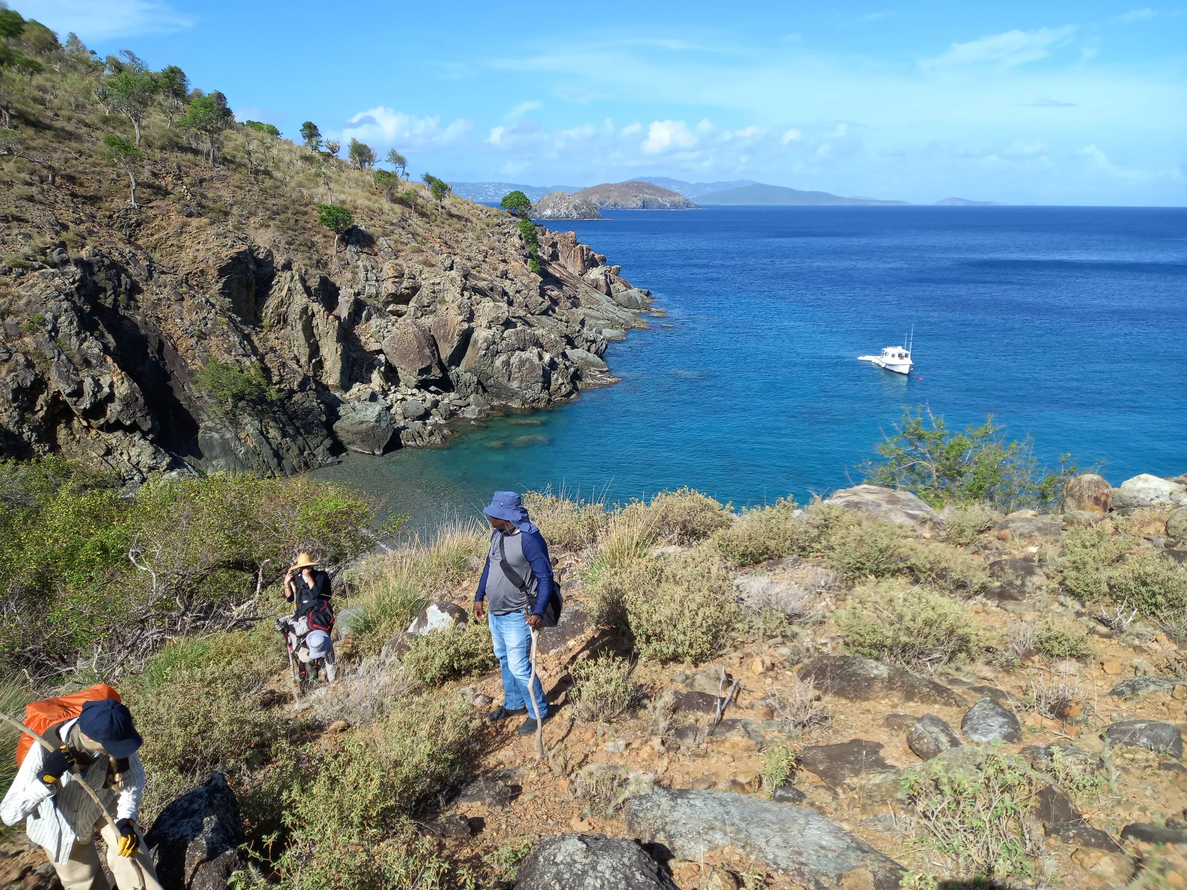 After disembarking from a dinghy, the team hike a ridge to begin work © RBG Kew Team in a setting of rock and scrub with the sea in the background