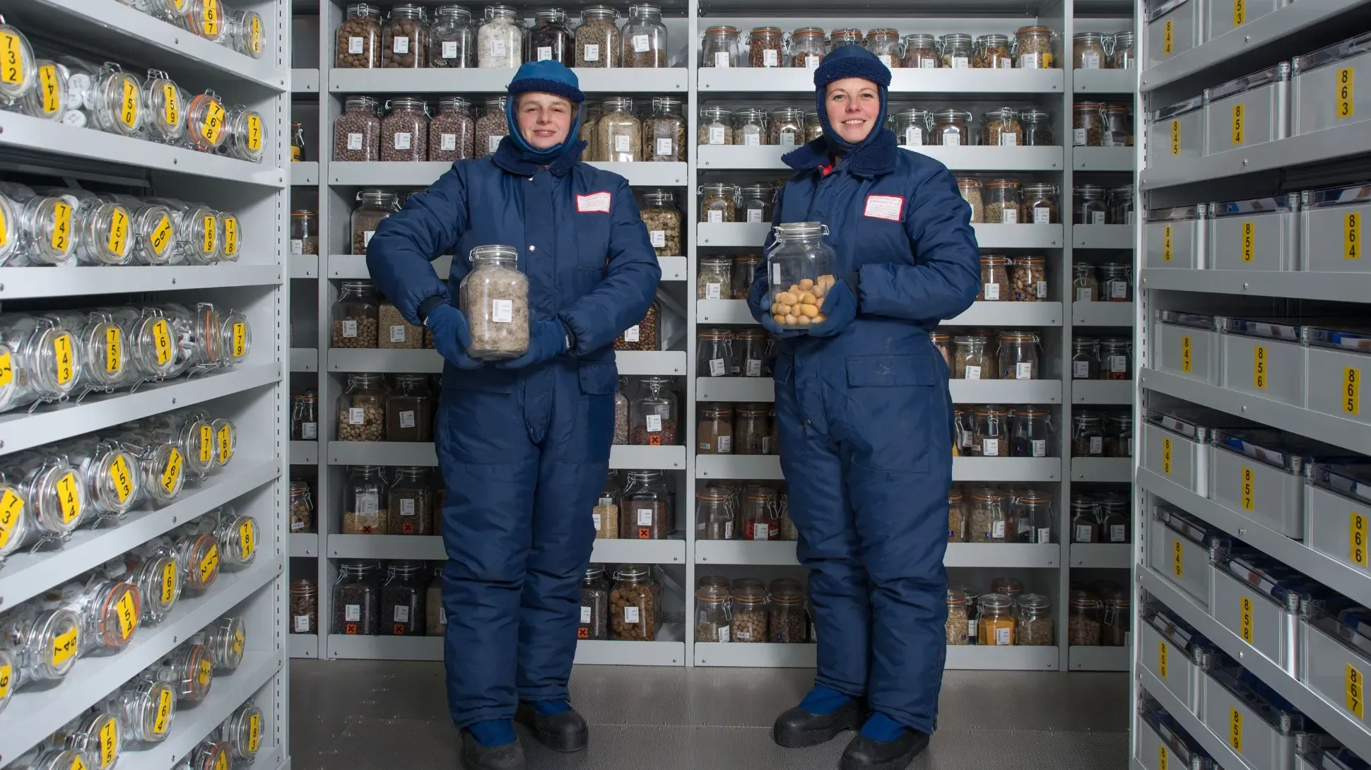 Scientists in the Millennium Seed Bank vault, Andrew McRobb © RBG Kew Two scientists in blue suits holding jars in the vault of the Millennium Seed Bank